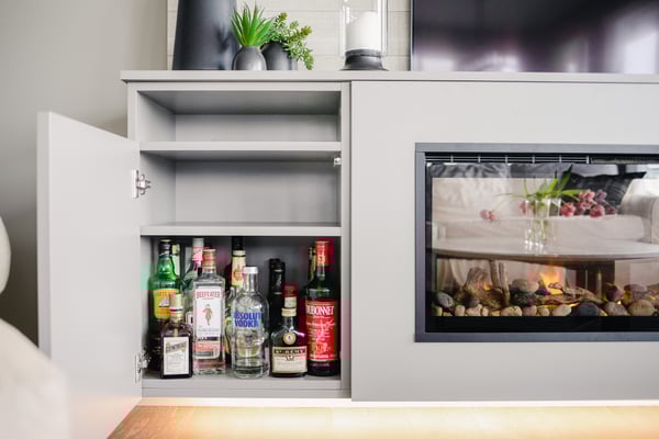 An open cabinet showing a collection of liquor in the base of a media unit