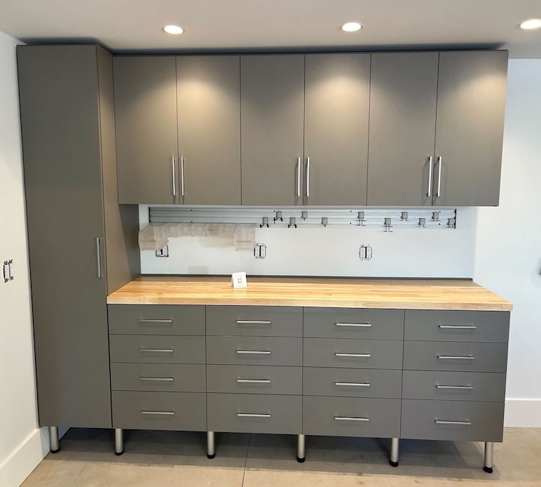 custom garage storage with grey cabinets, butcher block countertop, and fusion track wall