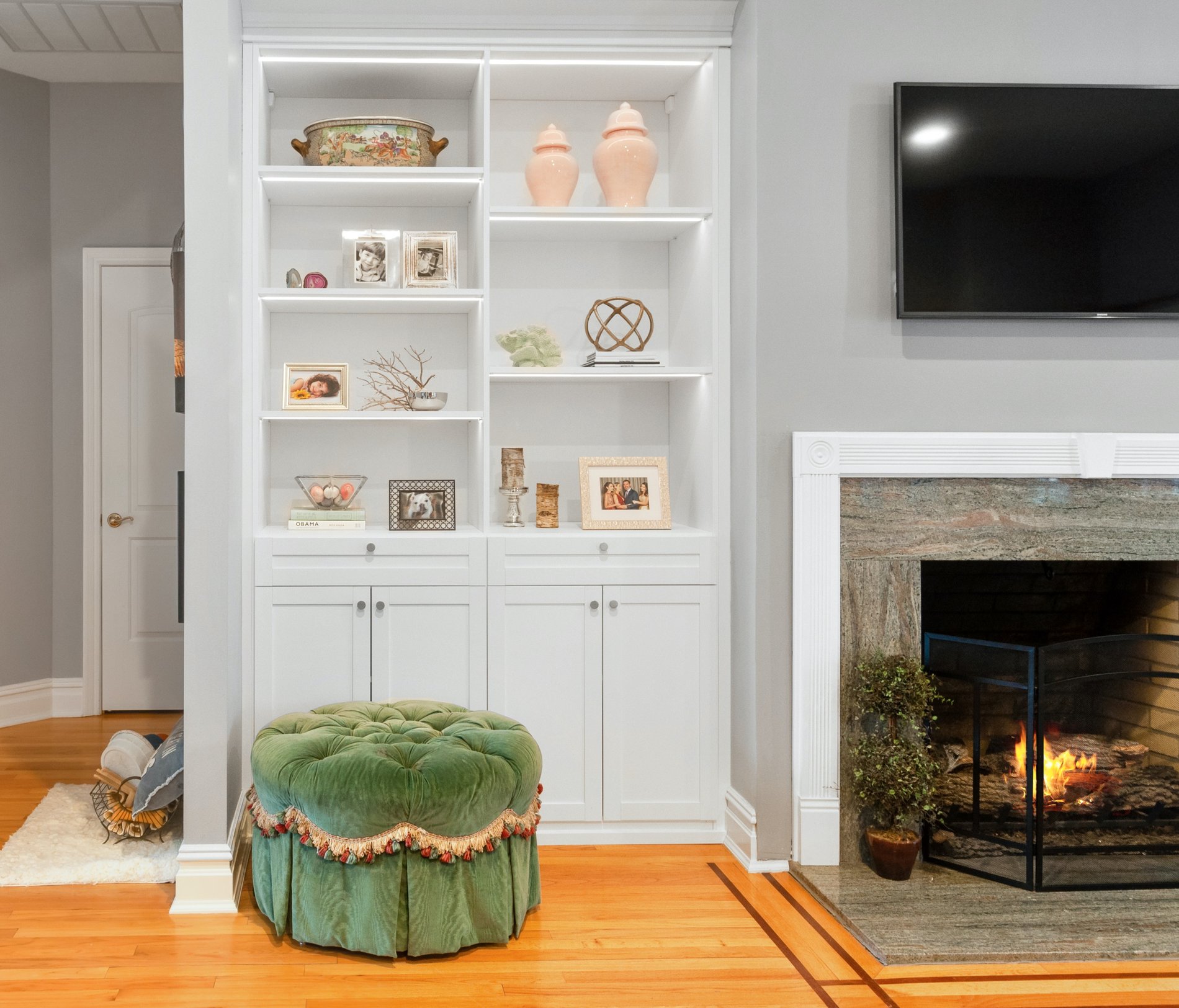 White built-in bookcase with green tufted stool next to fireplace with TV above itby California Closets Northern New Jersey.