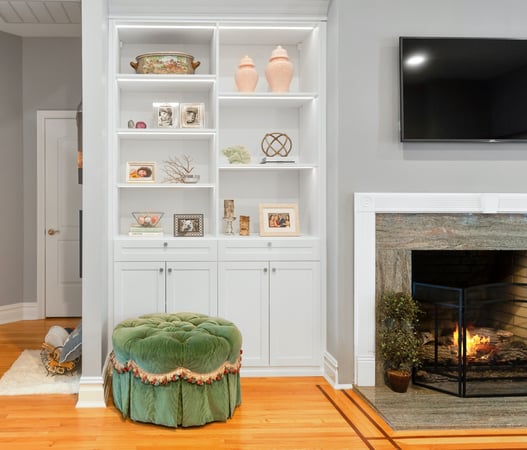White built-in bookcase with green tufted stool next to fireplace with TV above itby California Closets Northern New Jersey.