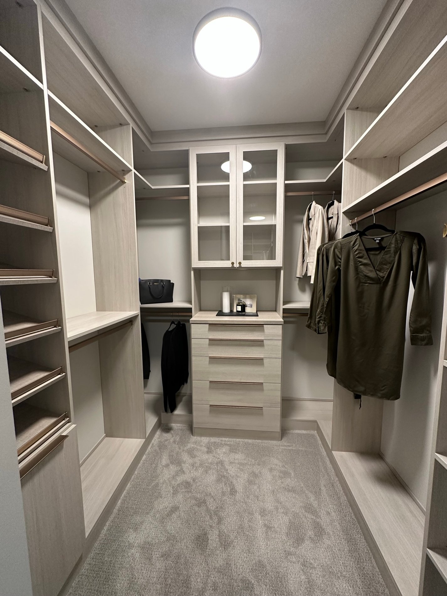 Light gray walk-in closet with gold hardware, hanging, open shelving, and drawers.