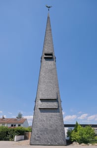 Schwarzer Kirchturm der Kirche in Ingelheim vor blauem Himmel.