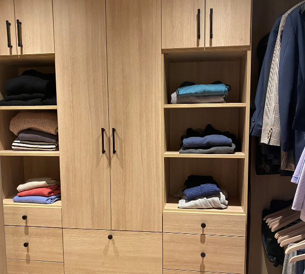 California Closets Westchester NY walk in closet. Natural oak wood color with black hardware for a modern neutral look with open and closed storage space, shelving, double hanging and drawers