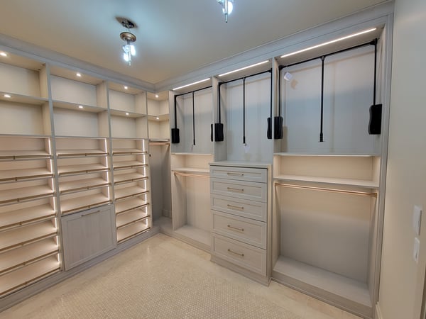Walk-in closet designed in a light wood grain finish. Closet features, double hanging, pull down bars for easy access, slanted shoe shelves, open shelving, drawers, pull out hamper, and lighting.