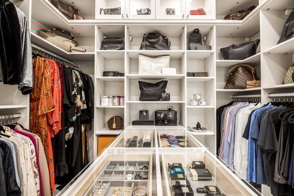 White walk-in closet with an island, shelving for displaying special items, and different levels of hanging.