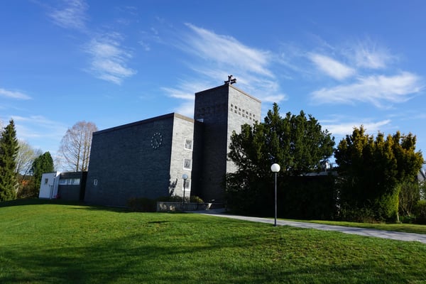 Das Bild zeigt die Evangelische Kirche Alsfeld-Eifa von außen. Die Fassade ist in grauen Ziegelsteinen gehalten. Die Kirche ist von Bäumen und einer Wiese umgeben.