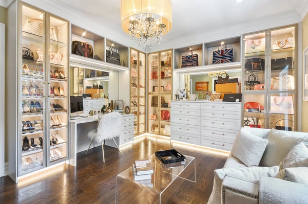 Glamorous dressing room with white cabinets, glass doors, vanity and sitting area by California Closets Northern New Jersey.