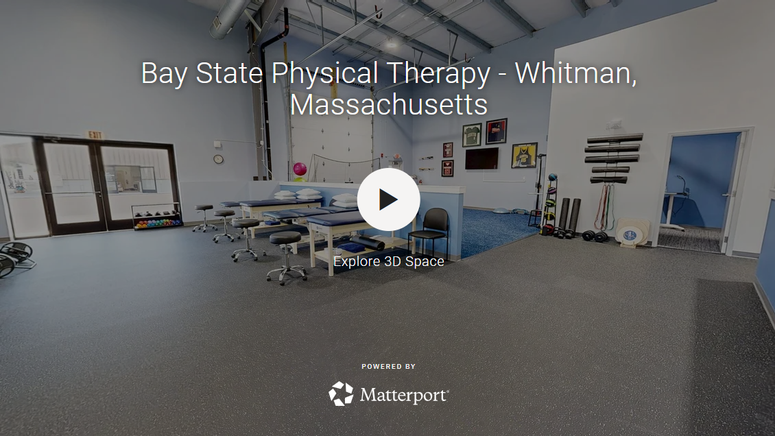Bay State Physical Therapy in Whitman, Massachusetts, is located at 263 Bedford Street. This single-floor physical therapy facility is designed to support comprehensive rehabilitation and athletic performance. The main gym area is expansive and open, boasting soaring ceilings with exposed steel beams, large windows that invite natural light, and a durable speckled rubber floor. Multiple treatment tables are positioned throughout the open floor for patient care. A dedicated exercise zone is equipped with a treadmill, weight bench, cable machine, resistance bands, and free weights, catering to a range of therapeutic exercise programs and additional functional fitness equipment including a cable/pulley system, balance tools, and sports memorabilia-adorned walls. A sports practice area includes a golf-hitting net and a turf-style blue carpet, accessible via a large garage-style door. Private treatment rooms offer adjustable therapy tables in a calm, softly lit setting. The facility also includes two accessible ADA-compliant restrooms with light wood-look flooring, grab bars, and clean white finishes throughout. The overall design is clean, professional, and purpose-built for clinical and athletic rehabilitation, empowering patients to move better, feel better, and live better.