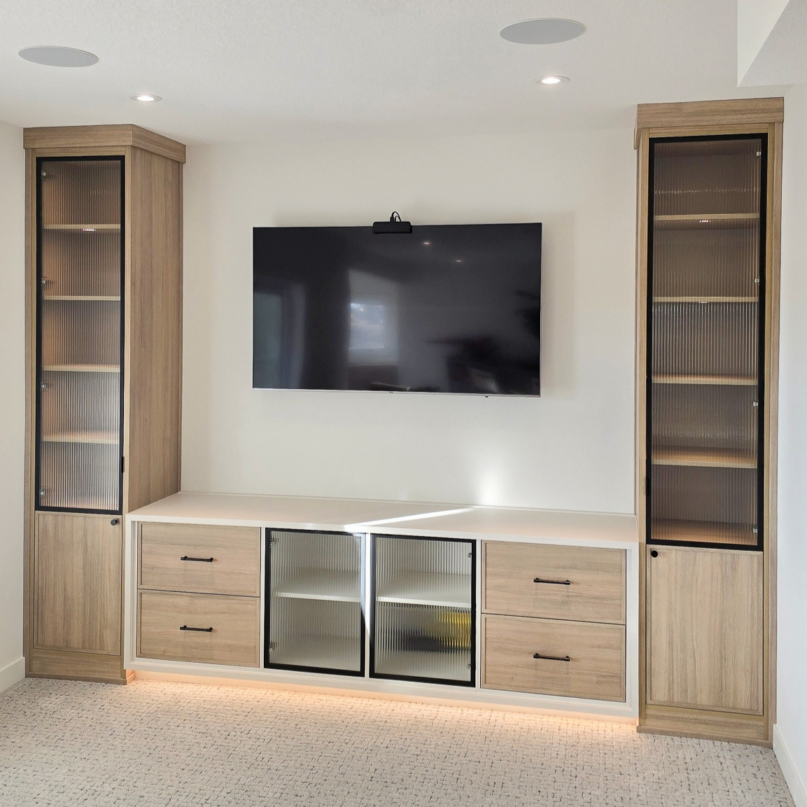 Media centre with lower middle storage, tower storage on both sides, toe kick lighting, and reeded glass.