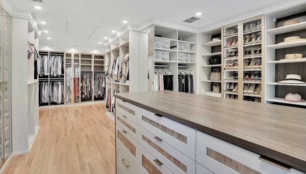 large walk-in closet with wood floors, white and brown island and hanging and shelves