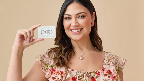 Woman wearing a plus size paisley printed blouse is smiling and holding up a Cato Fashions gift card.