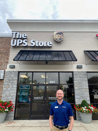 Smiling man in navy blue shirt standing outside, in front of The UPS Store