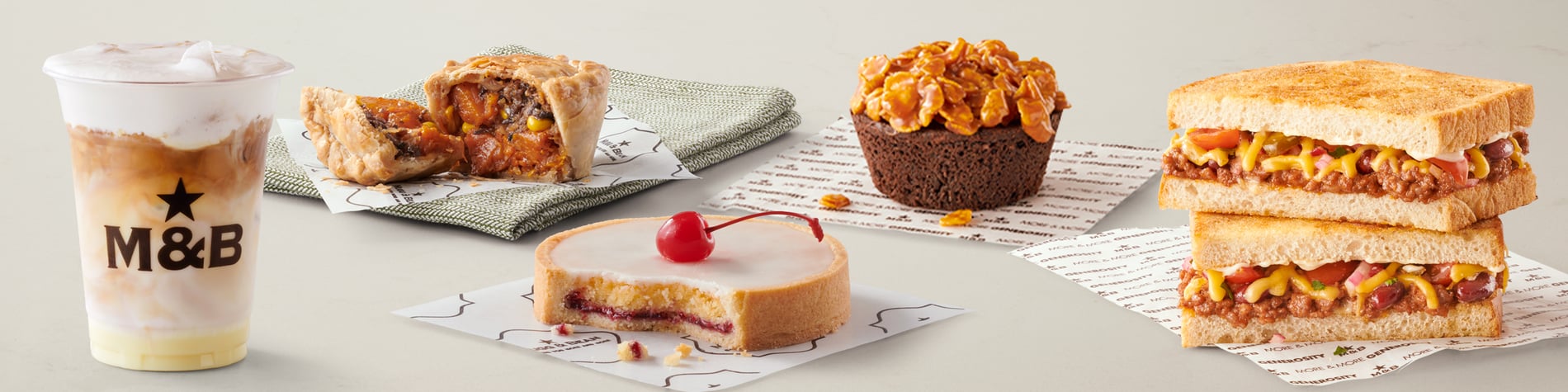 A selection of takeaway meals from the Mugg & Bean On-The-Move menu including a Mexican Chicken Toasted Sandwich, vegetarian Pot Pie, Gingerbread Latte hot drink, freshly baked citrus & ginger muffin, and a slice of Cherry Bakewell Tart.