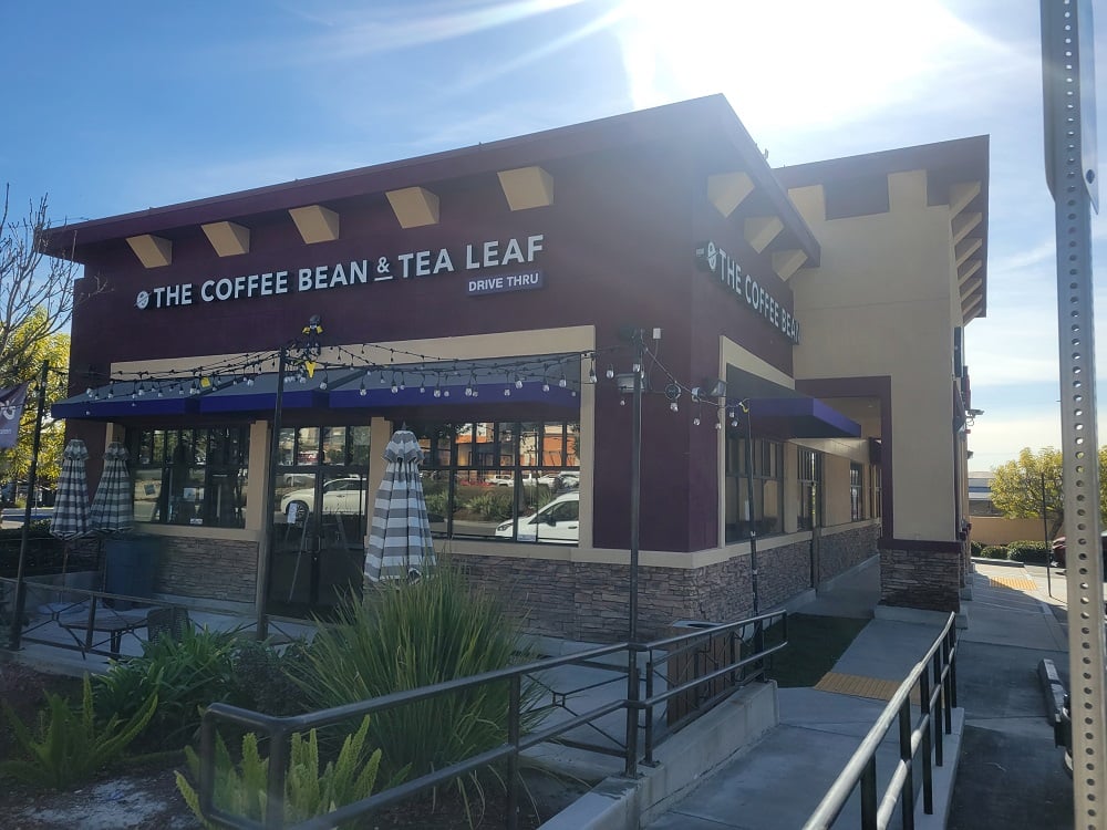 A store front of a drive thru The Coffee Bean & Tea Leaf showing outdoor seating, surrounded by palm trees and nice CA weather