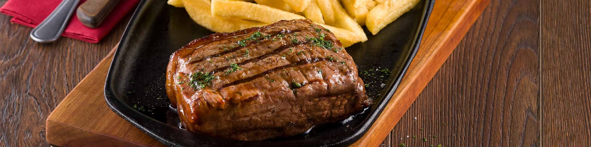 250g sirloin steak with chips served on a wooden board against a wooden background.