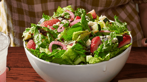 A bowl of our Strawberry Summer Salad featuring romaine, mixed greens, sherry dijon vinaigrette, pickled red onions, cucumbers, gorgonzola, strawberries,  and balsamic-fig glaze.