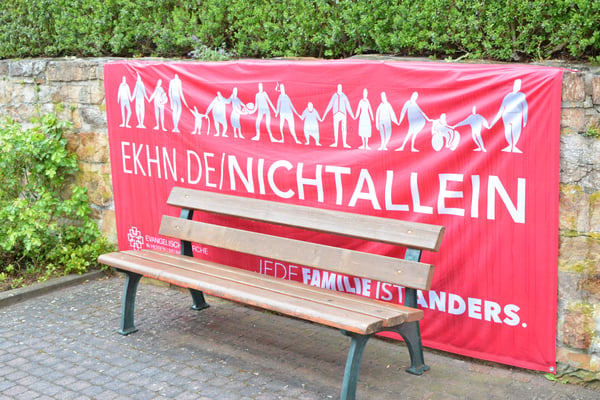 Eine Sitzbank vor einer Bruchsteinmauer. An der Mauer hängt ein Banner mit der Aufschrift "Du bist nicht allein"