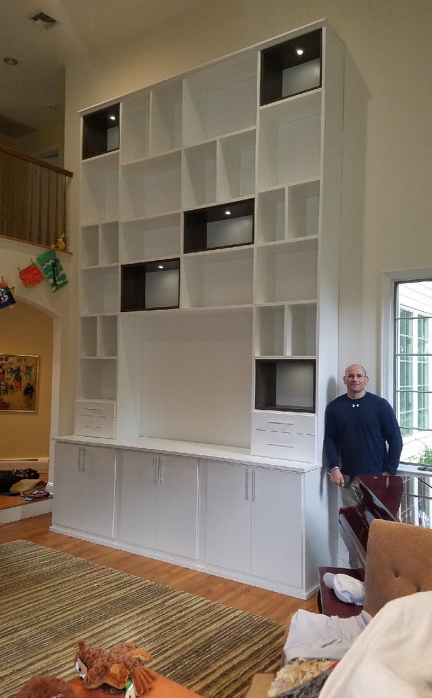 very tall entertainment center in white with cabinets underneath and man standing next to it