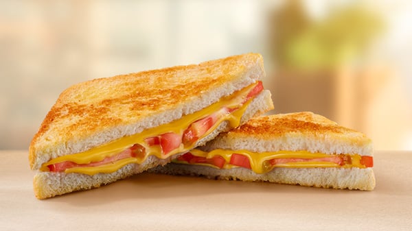 A Cheese & Tomato Toasted Sandwich on a brown surface with a blurred background.