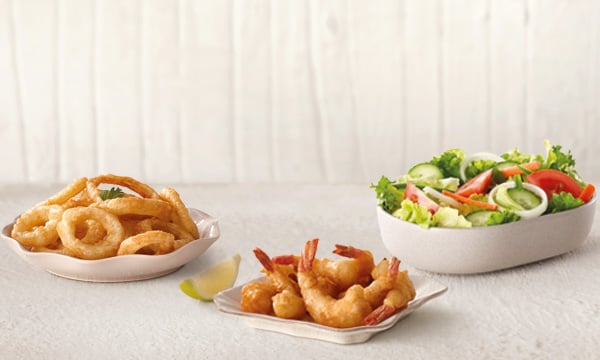 Onion rings, battered and deep-fried prawns, and a Greek salad on a white background