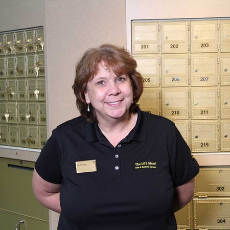 Smiling The UPS Store owner in front of mailboxes