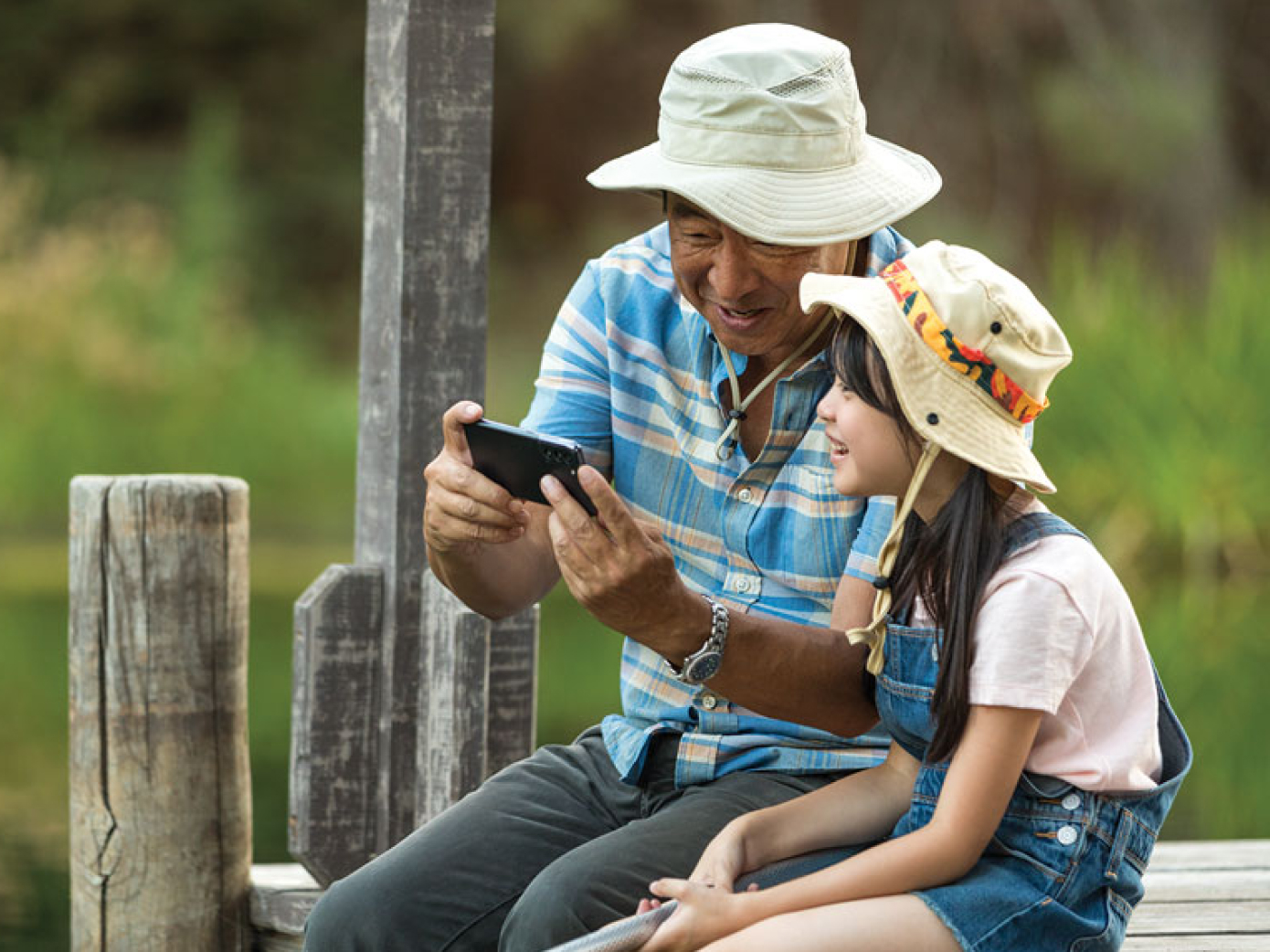 Man and daughter look at phone together while sitting on a dock