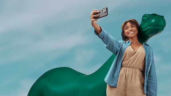 Girl smiling and standing next to Dinosaur statue taking a selfie with a cell phone.