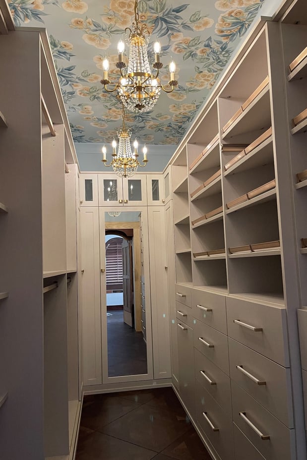 Narrow custom walk-in closet with floor-to-ceiling shelving, built-in drawers, wardrobe storage, and decorative ceiling details.
