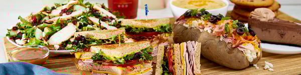 A spread of McAlister's menu items, consisting of the Savannah Chopped Salad, King Club Sandwich, Spud Max, Godiva Double Chocolate Cheesecake, Chocolate Chip Cookies and Broccoli and Cheddar Soup