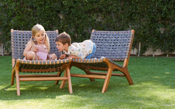 two kids in backyard sitting on lawn chairs using a tablet