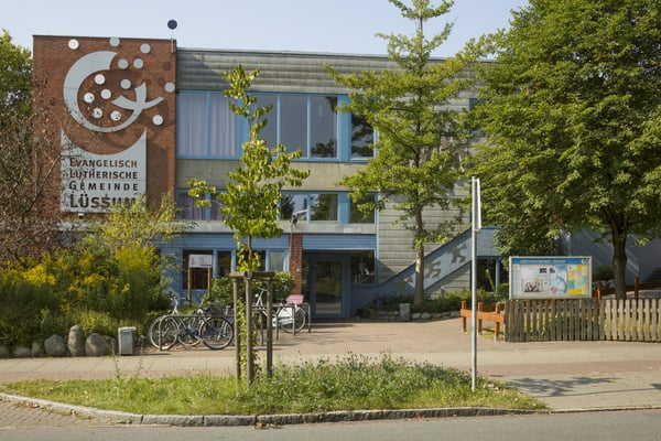 Ein modernes Kirchengebäude umringt von neu gepflanzten und älteren Bäumen.
