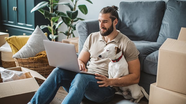 Man sitting with a dog looking at a laptop.