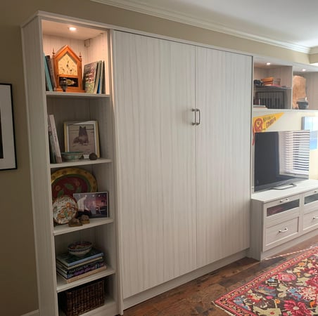 Grey wall-bed system with shelving and a television