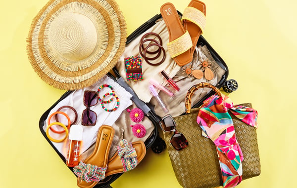 Accessories are displayed inside an open suitcase on top of a yellow background.