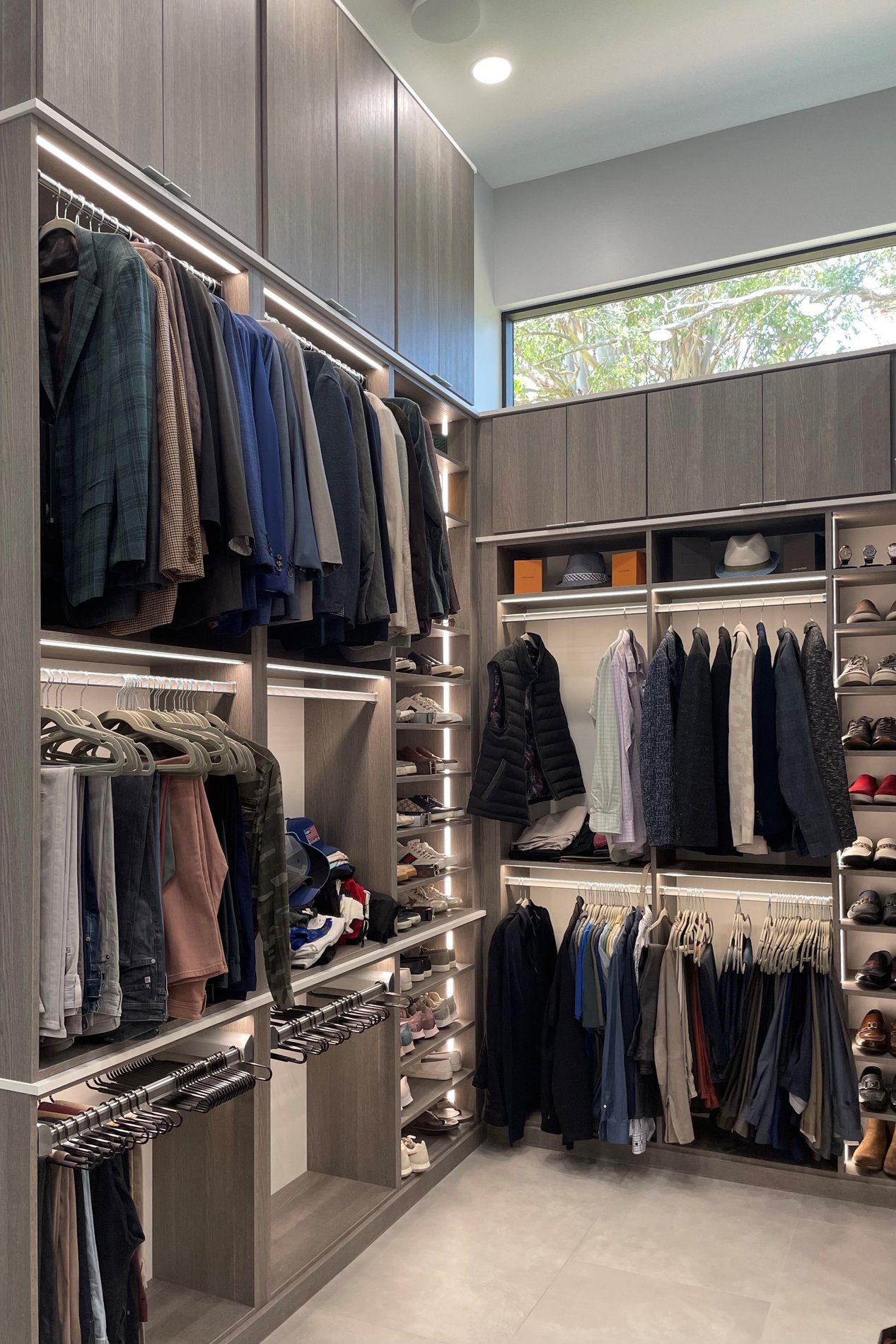 A three-tier walk-in closet in ash finish featuring integrated lighting, pant organizers, and sleek finger pulls.