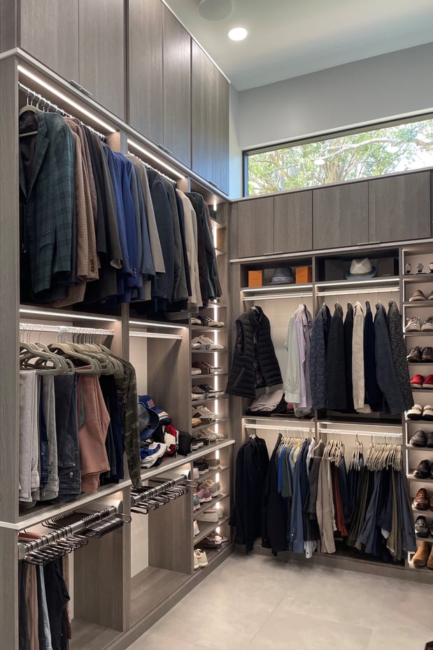 A three-tier walk-in closet in ash finish featuring integrated lighting, pant organizers, and sleek finger pulls.