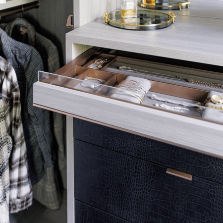 Everstyle accessory drawer with organized compartments above custom leather-front drawers in a luxury closet.