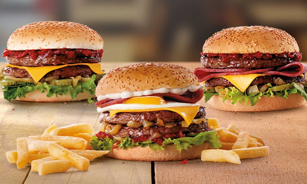 Three beef burgers in between two servings of chips on a wooden table.