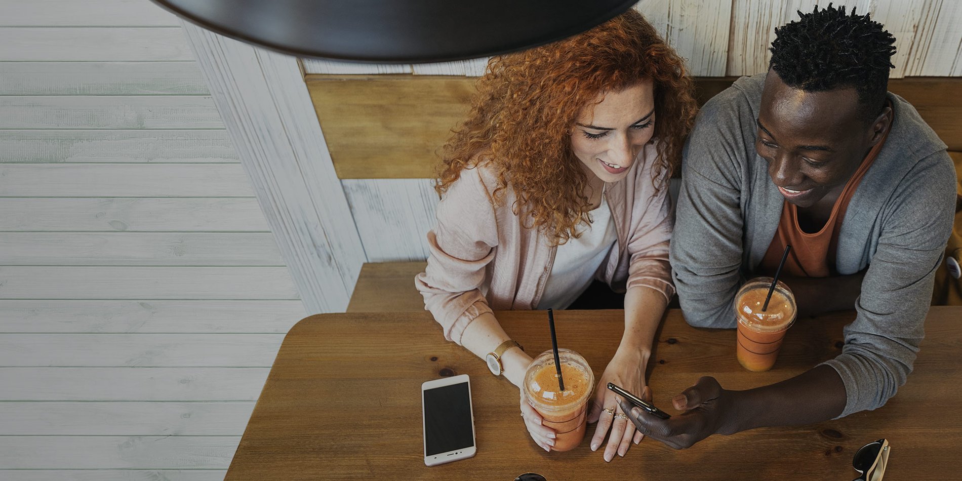 Foto de una pareja joven en una cafetería sonriendo a un teléfono inteligente conectado a Optimum Mobile