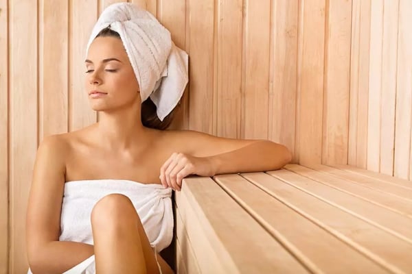 Woman sitting in sauna with towel on head