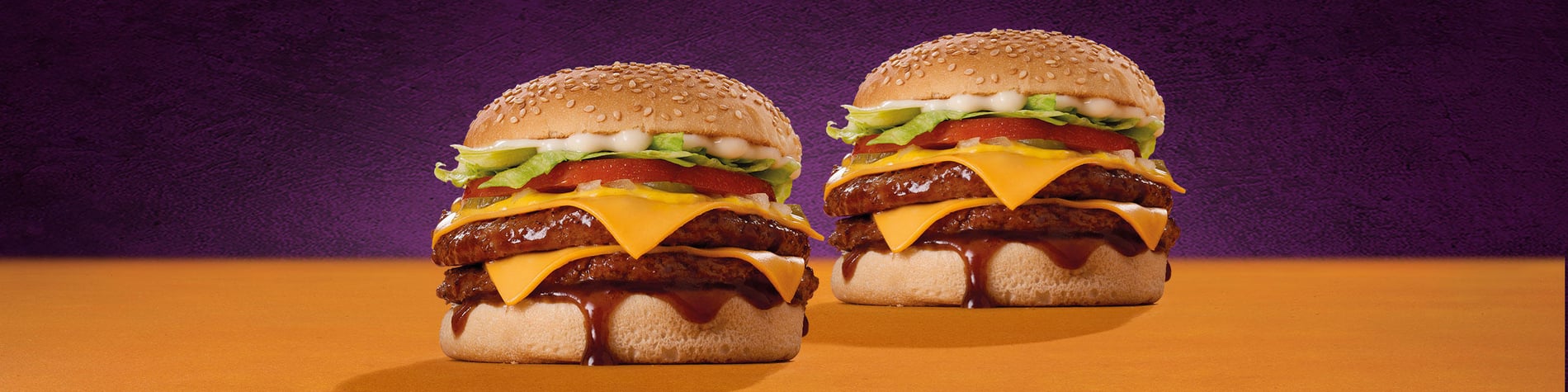 Flame-grilled Steers burger next to a full portion of chips against a purple background.