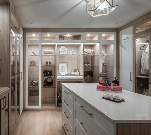 Img 1 California Closets Westchester County New York Two Toned White and Beige Large Walk-in Luxury Closet with Glass Shelving, Glass Doors, Lighting, and a Custom Center Island with Custom Jewelry Drawers