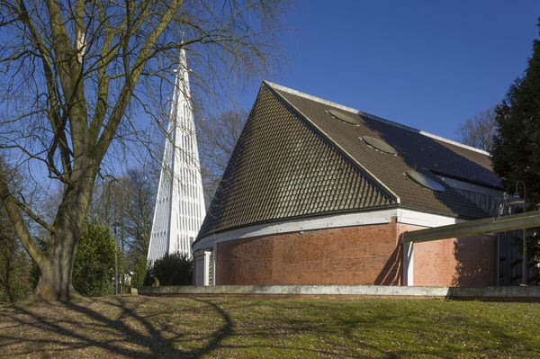 Ein modernes Kirchengebäude mit einem spitzzulaufenden, pyramidenförmigen Glockenturm.