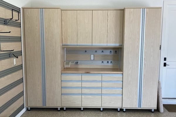 Custom garage storage system with light wood cabinetry, full-height cabinets, open shelving, drawers, and organized tool storage.