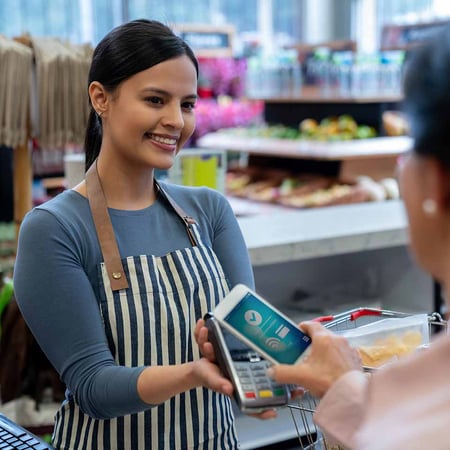 A woman holding up a payment processing tool. Another person is holding their photo to the payment machine.
