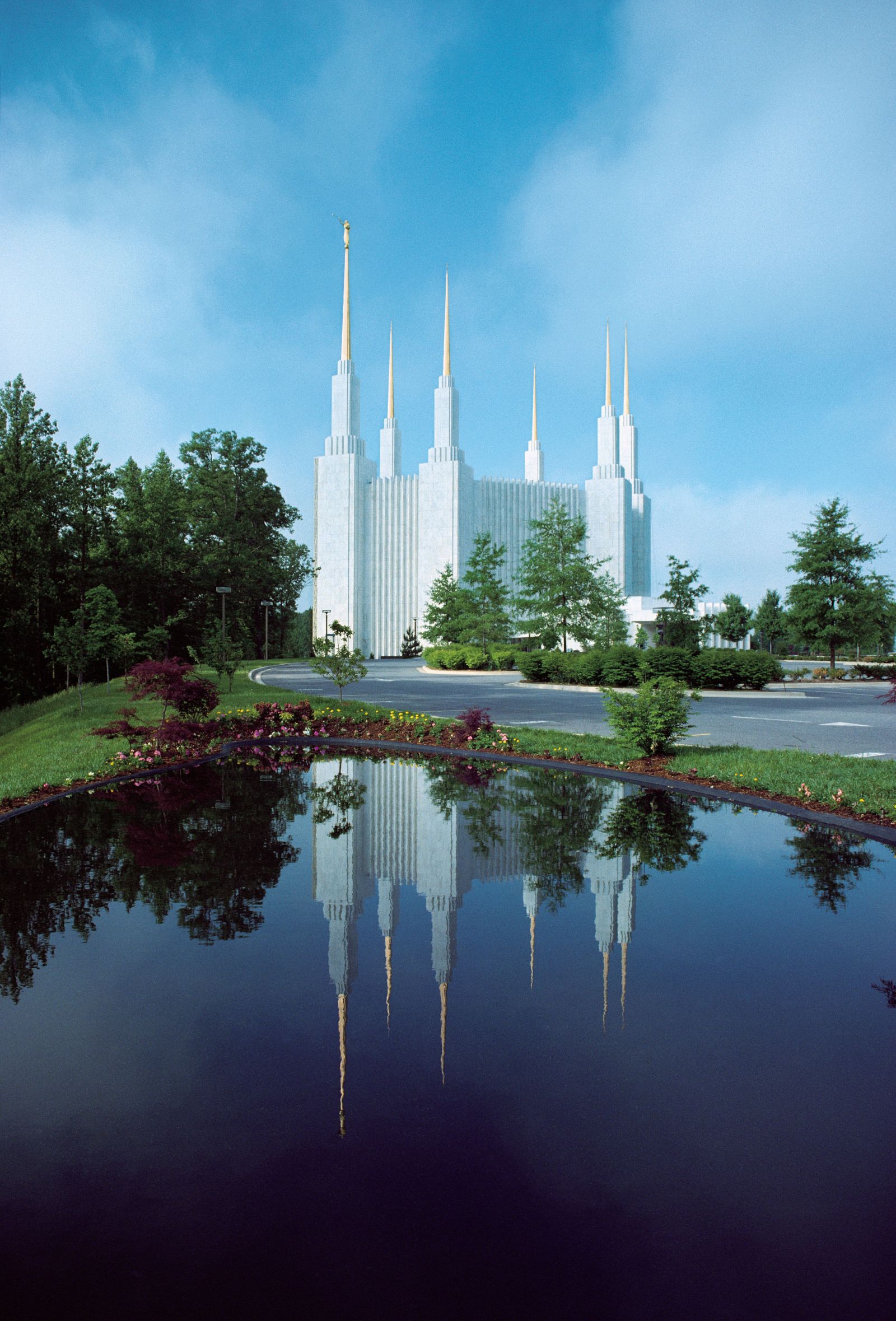 The D.C. Temple in the distance, the spires reach into the sky,. The  reflection of the temple and the surrounding trees is  is in the foreground.