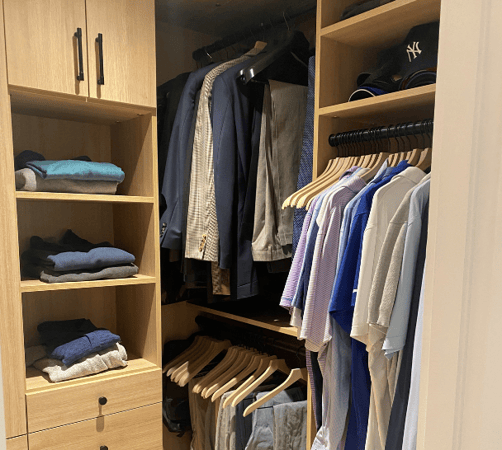 California Closets Westchester NY natural wood oak colored walk in closet with various hanging heights, shelving, cabinets and drawer space with modern black hardware
