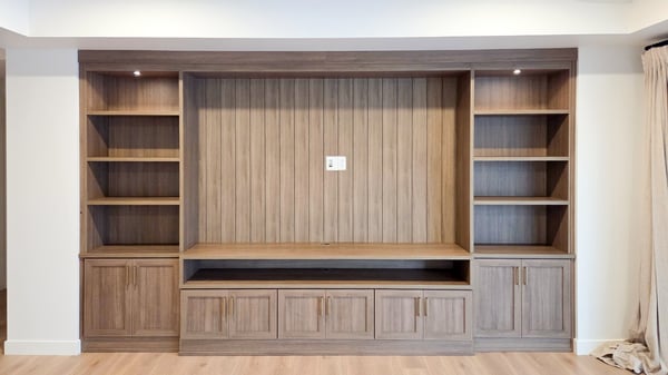 Media centre in a mid tone wood grain finish with open shelving, lighting, and closed storage.