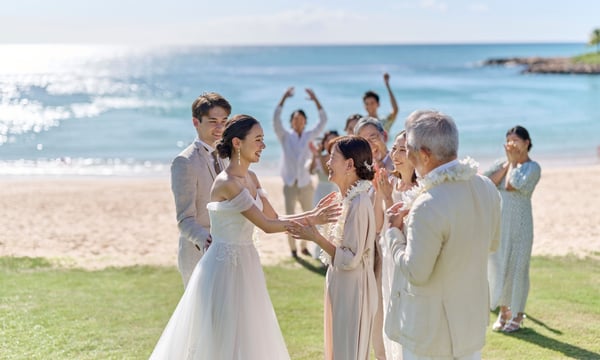 海辺で微笑みあう新郎新婦と両家家族