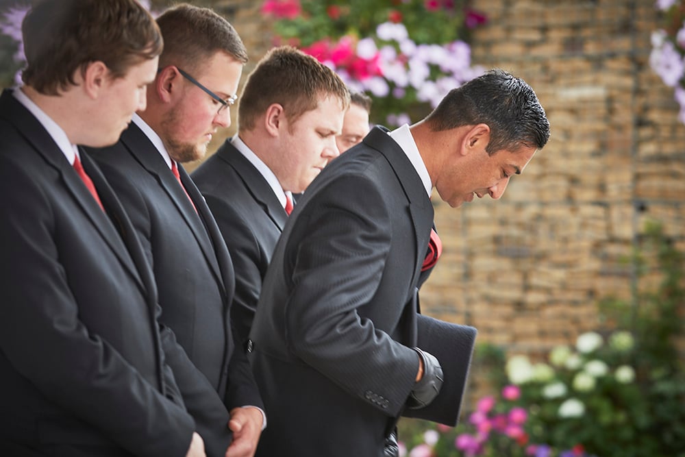 A team of funeral directors bow in respect at a funeral. The lead Funeral Director holds a top hat in his hands.